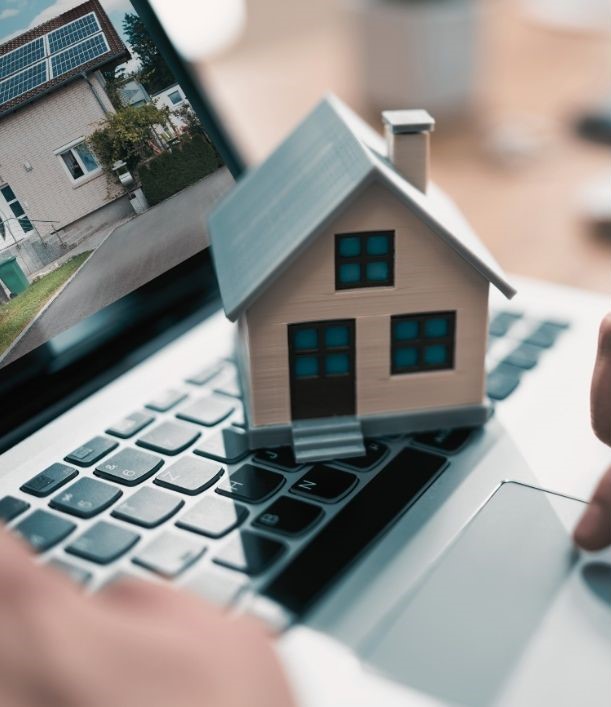 Modell eines Hauses auf einer Laptop-Tastatur mit einer Immobilienanzeige auf dem Bildschirm, symbolisierend den digitalen Immobilienankauf.